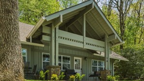 A two-story house with a covered porch, stone fireplace, and a stone chimney. - Wooded Highlands Cottage - Patios & Fireplace (Highlands)