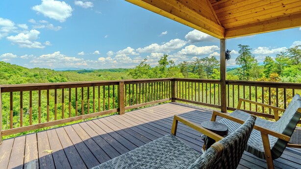 Eine Holzterrasse mit überdachtem Bereich, Korbmöbeln und Blick auf eine grüne Landschaft.