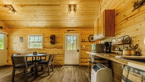 Ein Holzblockhaus-Innenraum mit Esstisch, Stühlen, einer Küchenzeile inklusive Herd und Kühlschrank.