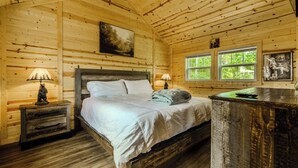 Ein Schlafzimmer einer Holzhütte mit einem Bett, zwei Nachttischlampen, einem Fenster und einer Holzkommode.