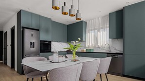 Een moderne keuken met blauwgroene kastjes, een marmeren aanrecht en een eethoek met een witte tafel en grijze stoelen.