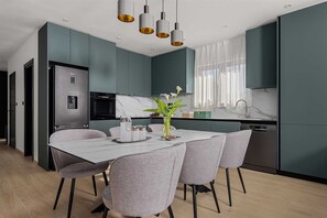 Eine moderne Küche mit türkisblauen Schränken, einer Marmorarbeitsplatte und einem Essbereich mit weißem Tisch und grauen Stühlen.