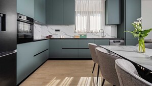 Een moderne keuken met donkere kastjes, een marmeren aanrecht en een eethoek met een tafel en stoelen.
