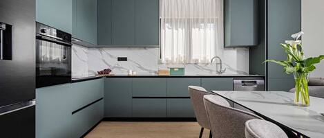 A modern kitchen with dark cabinetry, a marble countertop, and a dining area with a table and chairs.
