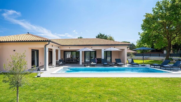 Een huis met een zwembad, terras en een verzorgd gazon.
