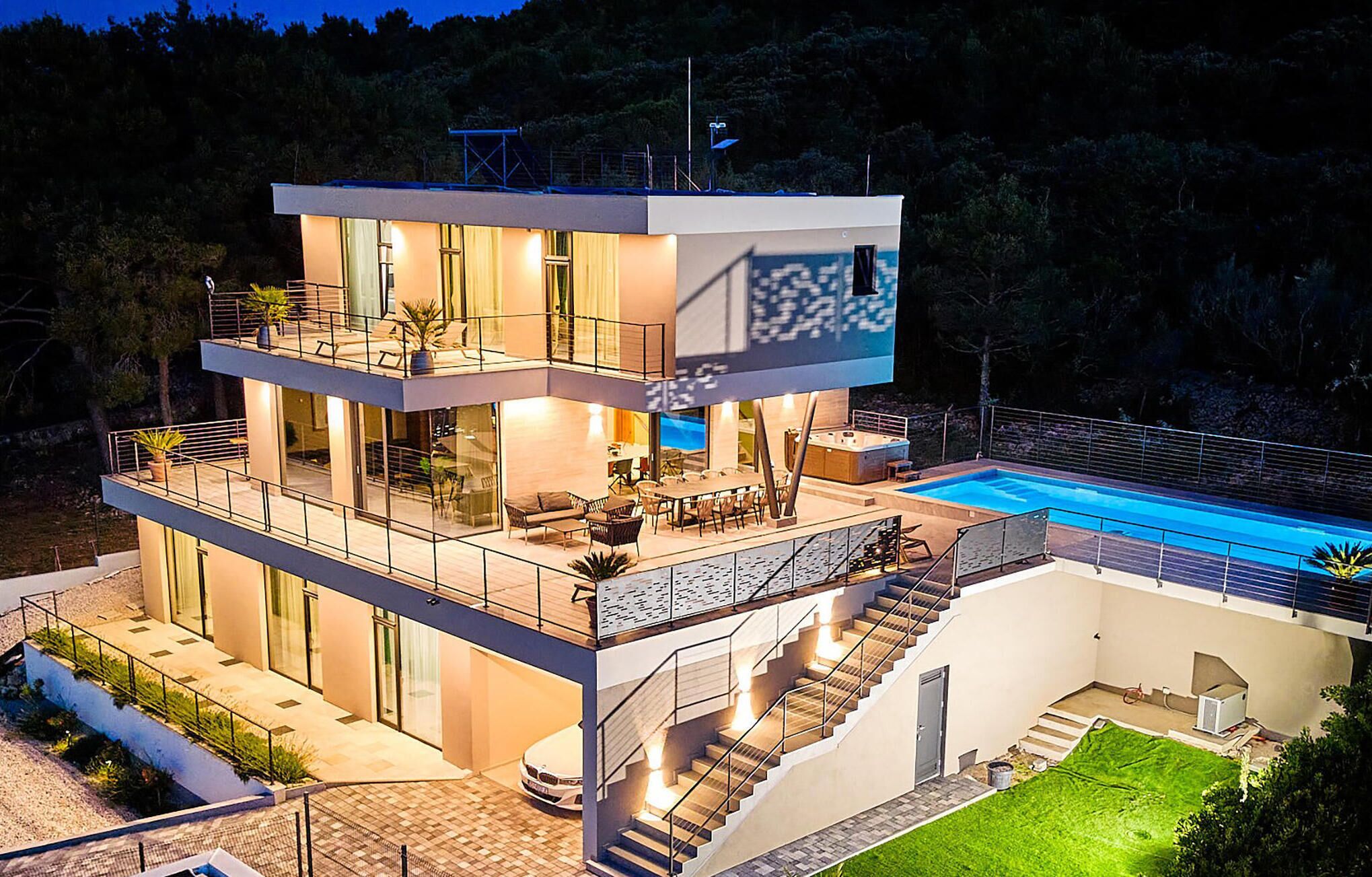 Ein modernes, zweistöckiges Haus mit Swimmingpool, Sitzgelegenheiten im Freien und einer Treppe, die zum oberen Stockwerk führt.