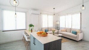 Ett modernt vardagsrum med en soffa, en matplats med stolar och en köksö med frukt.