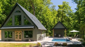 Une maison à deux étages dotée d’une grande véranda à l’avant, d’une piscine et d’un espace extérieur aménagé et couvert.