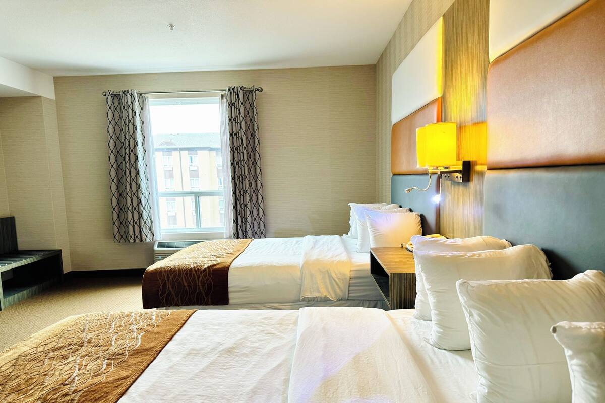 Una habitación de hotel con dos camas, una mesita de noche, una lámpara y un ventanal con cortinas.
