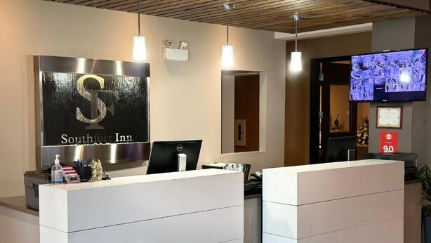 A reception desk with a large illuminated sign, a flat-screen TV, and a digital display. - Southfort Inn  (Fort Saskatchewan)