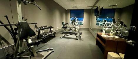 Un gimnasio con equipo de ejercicio, una recepción y un ventanal amplio.