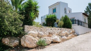 Um edifício branco com um muro de pedra, palmeiras e céu claro.