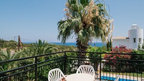 Uma varanda com mesa e cadeiras, vista para uma piscina e o mar.