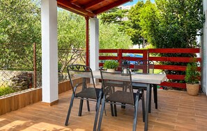 Eine Terrasse im Freien mit Tisch und Stühlen, umgeben von einem roten Zaun und Grünpflanzen.