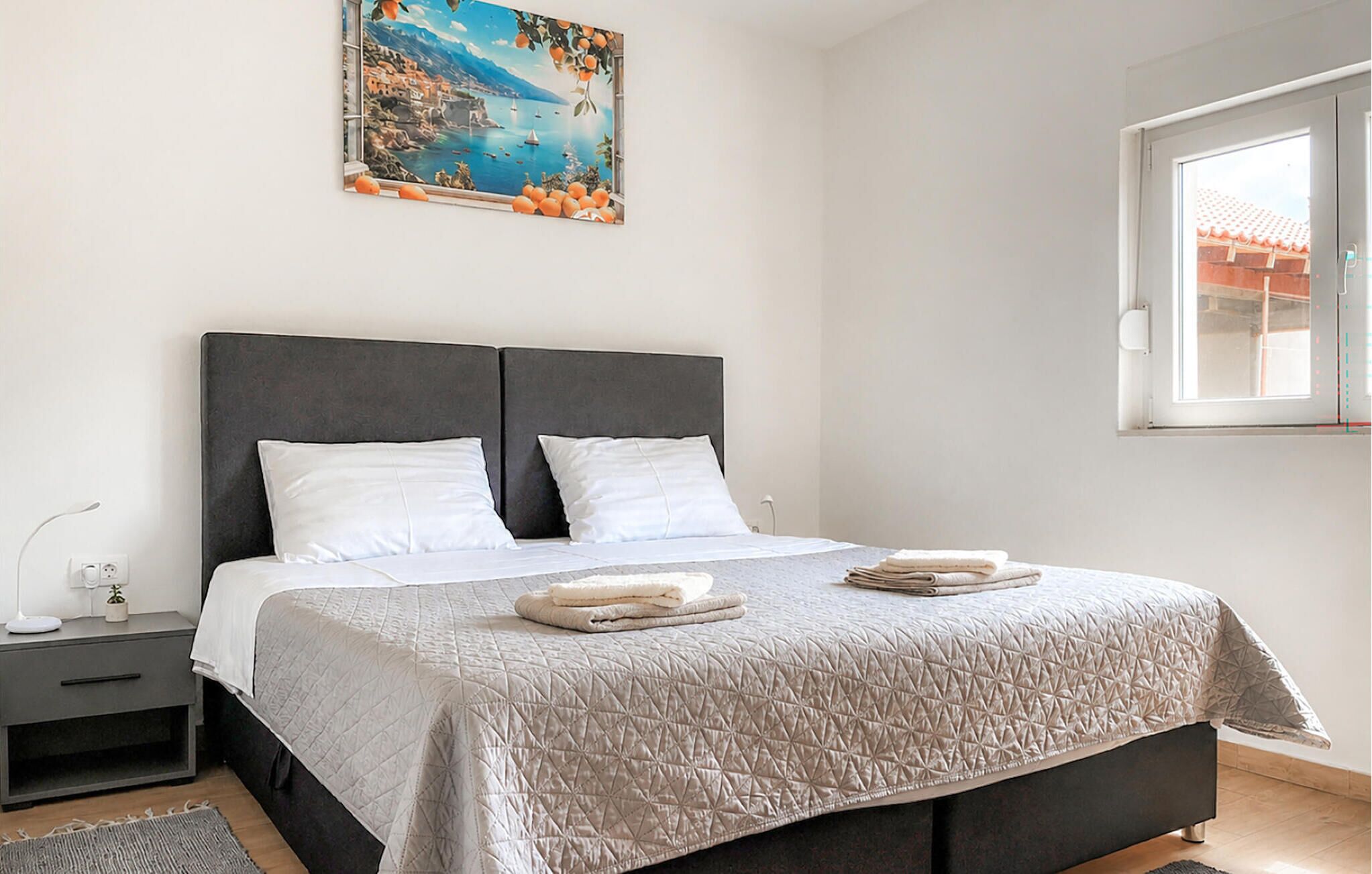 Une chambre à coucher avec un lit, deux oreillers, une table de chevet, une lampe, un tableau et une fenêtre.