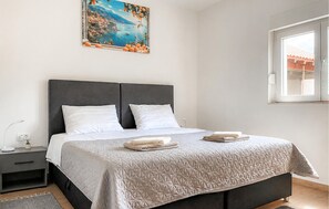 Ein Schlafzimmer mit einem Bett, zwei Kissen, einem Nachttisch, einer Lampe, einem Gemälde und einem Fenster.