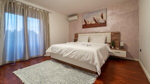 A bedroom with a bed, a nightstand, a wall-mounted air conditioner, and a window with curtains. - Beautiful home in Donje Rastane (Donje Rastane)