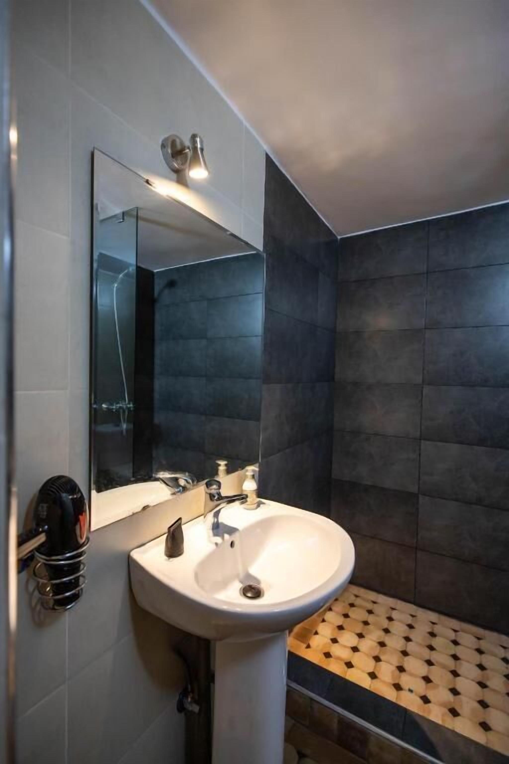 A bathroom with a white sink, a mirror, and dark tiled walls.