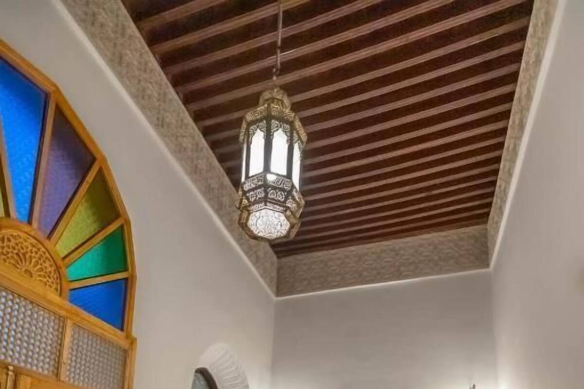 A room with two beds, a patterned rug, a wooden door with a geometric design, and a hanging lantern.