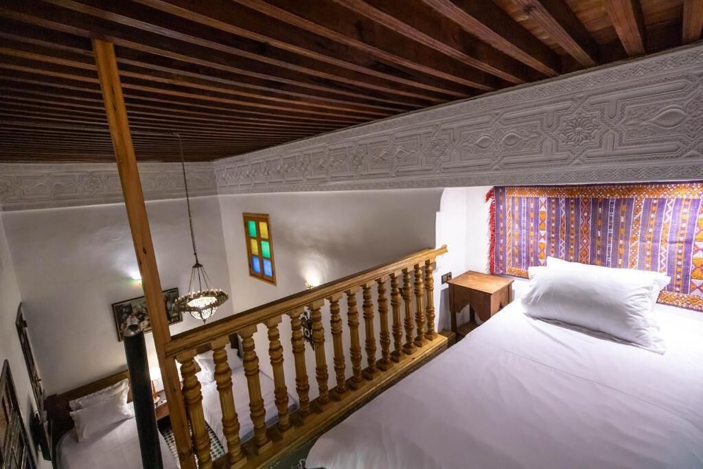 Un dormitori amb una escala de fusta, un llit amb roba de llit blanca, una petita taula de nit i una finestra amb cortines estampades.