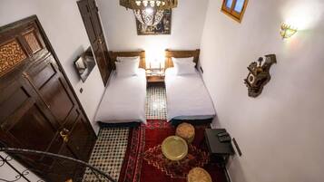 Une chambre avec deux lits, un lustre, un tapis à motifs, une petite table et une horloge murale.