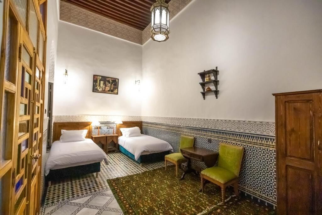 A room with two beds, a small table, a chair, and a cabinet.