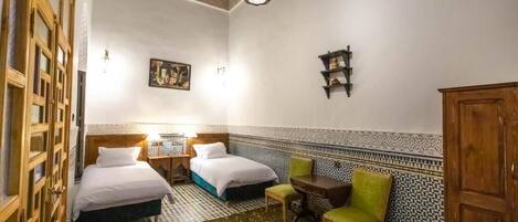 A room with two beds, a small table, a chair, and a cabinet.