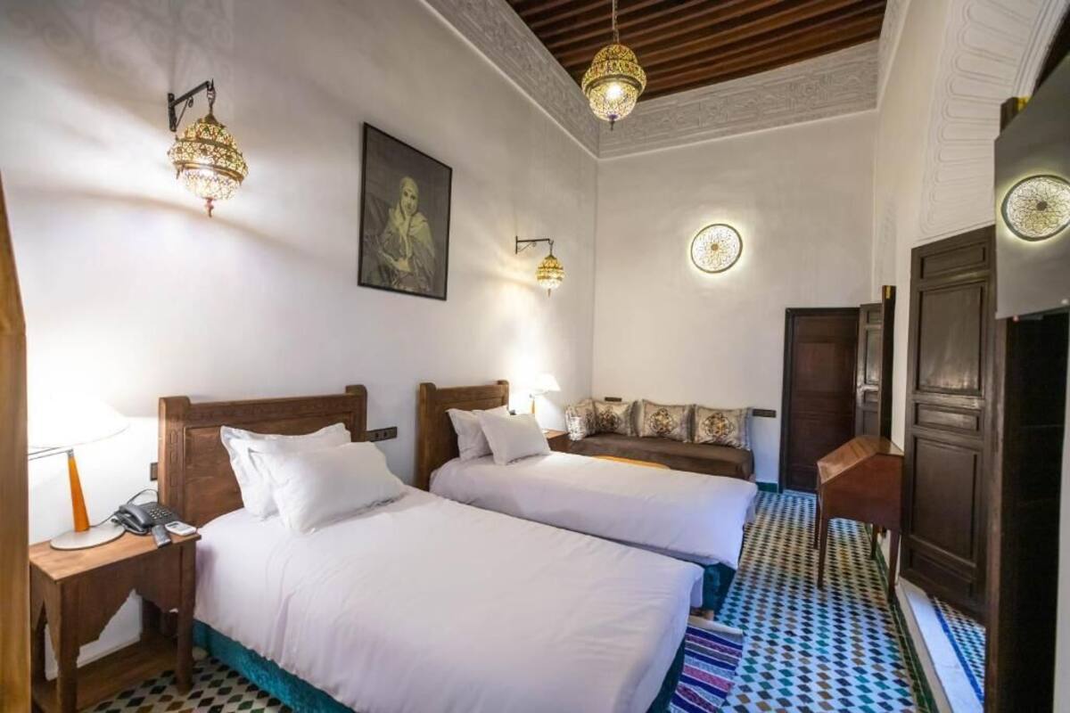 A hotel room with two beds, a wooden headboard, a patterned floor, and decorative wall sconces.