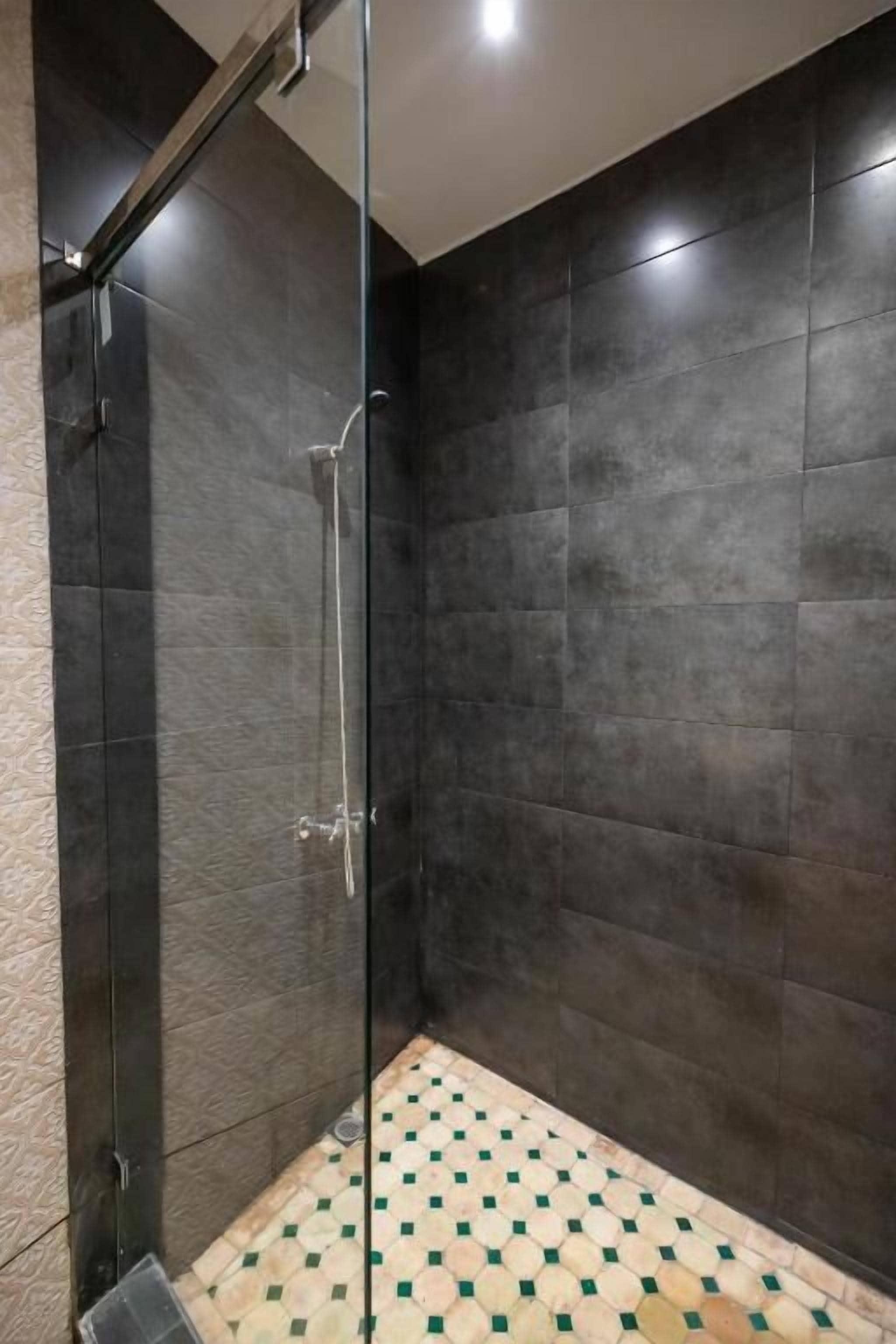 Ducha con azulejos oscuros y piso estampado.