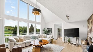 Ein geräumiges Wohnzimmer mit großem Fenster, einem modernen Sofa, einem Holztisch und einem Flachbildfernseher.