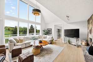 Ein geräumiges Wohnzimmer mit großem Fenster, einem modernen Sofa, einem Holztisch und einem Flachbildfernseher.