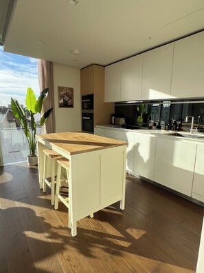 A modern kitchen with white cabinets, a wooden dining table, and a potted plant. - The Brompton Residence (London)