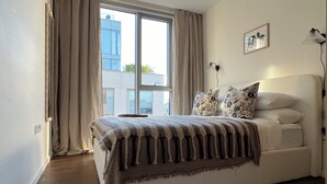 A bedroom with a large window, a bed with patterned bedding, a bedside lamp, and a framed picture on the wall. - The Brompton Residence (London)
