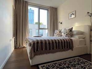 A bedroom with a large window, a bed with patterned bedding, a bedside lamp, and a framed picture on the wall. - The Brompton Residence (London)