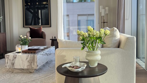A modern living room with a marble coffee table, a beige sofa, a large abstract painting, and a view of a building through a window. - The Brompton Residence (London)