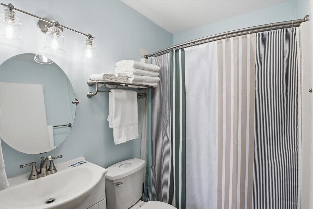 A bathroom with a sink, mirror, towel rack, toilet, and a shower curtain.