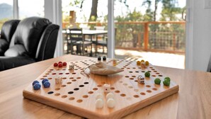 A wooden board game with dice and tokens on a table, set in a room with a view of a balcony and outdoor furniture. - Marina View Cabin - Boat Slip - Sleeps 11 - Pets OK (Bass Lake)