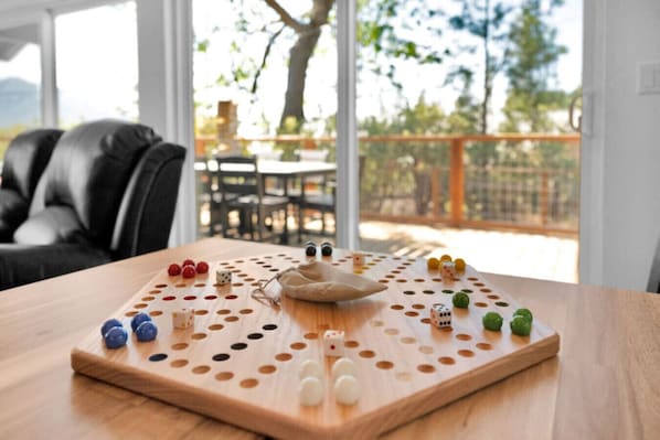 Un juego de mesa de madera con dados y fichas sobre una mesa, situado en una habitación con vistas a un balcón y muebles de exterior.