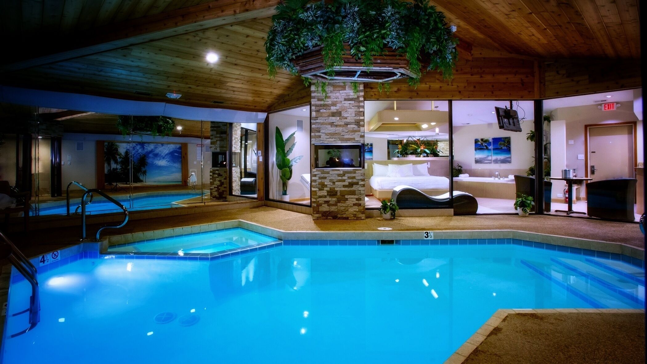 An indoor swimming pool with a stone wall, a bed, and a bathroom.