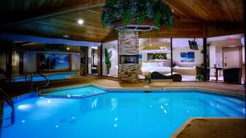 An indoor swimming pool with a stone wall, a bed, and a bathroom.