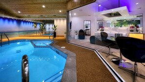 A modern indoor pool area with a glass partition, a seating area with a sofa and chairs, and a view of the pool through the partition. - Sybaris Pool Suites Frankfort (Frankfort)