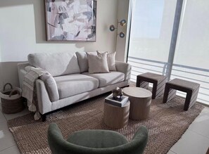 Ein Wohnzimmer mit einer Couch, zwei runden Couchtischen, einem kleinen Beistelltisch, einem Sessel und einem großen Fenster.