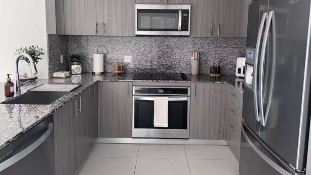 Une cuisine moderne avec des meubles gris, un réfrigérateur en acier inoxydable, un four à micro-ondes et un four traditionnel.