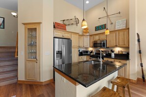 A kitchen with wooden cabinets, a stainless steel refrigerator, a microwave, and a large island with stools. - Downtown WP River Villa 522 I Private Hot Tub I Great Views I Work Station I Discounted Attractions (Winter Park)