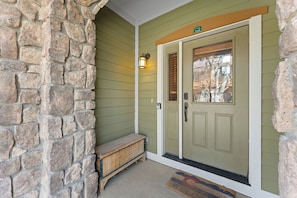A stone wall, a wooden bench, a green door with a window, and a welcome mat. - Downtown WP River Villa 522 I Private Hot Tub I Great Views I Work Station I Discounted Attractions (Winter Park)