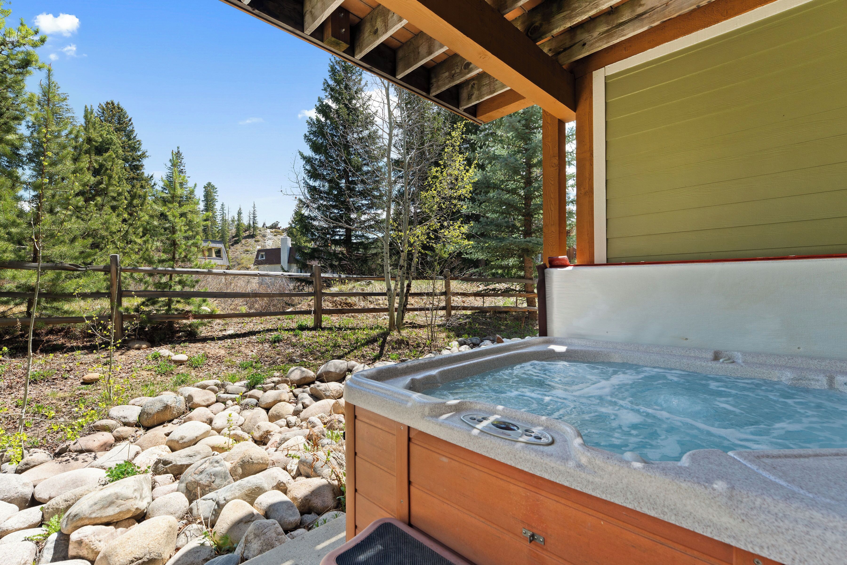 A hot tub outdoors with a wooden deck, a stone pathway, and a wooden fence.
