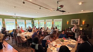 A dining area with multiple tables and chairs, a ceiling fan, and large windows.