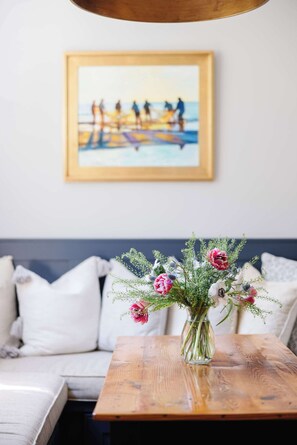 Ein Holztisch mit Blumenvase, eine Couch mit Kissen und ein gerahmtes Bild an der Wand.