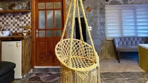 A rustic interior with a hanging macrame chair, wooden beams, stone walls, a checkered tile backsplash, and a stone fireplace.