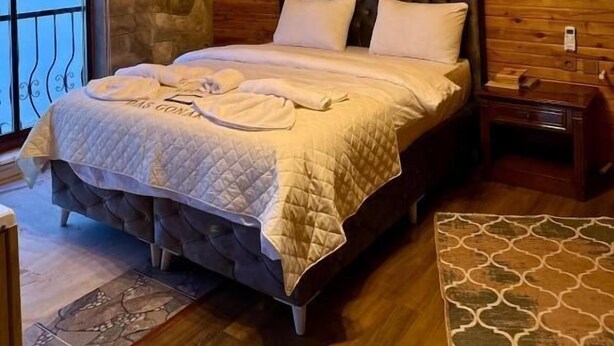 A wooden room with a bed, a stone wall, and a chandelier.